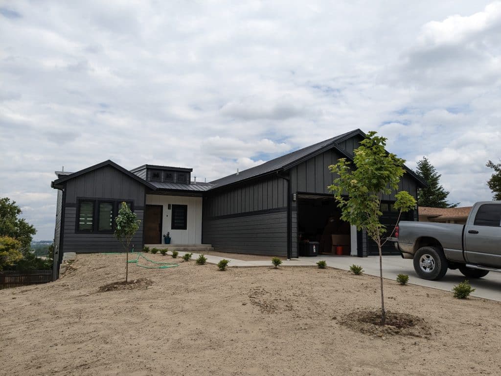 PXL_20230615_193858139 Modern dark gray home with white trim, new landscaping, and a truck in the driveway.