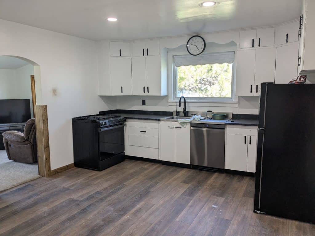 Bright Kitchen White Cabinets Black Appliances Bright kitchen with white cabinets, black appliances, wood-look flooring, and a window with natural light.