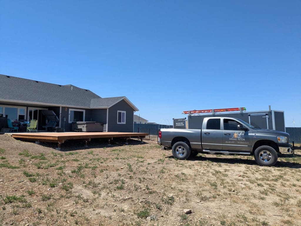 House With New Deck Grand Teton Construction Truck Gray Grand Teton truck parked near a new wooden deck and house.