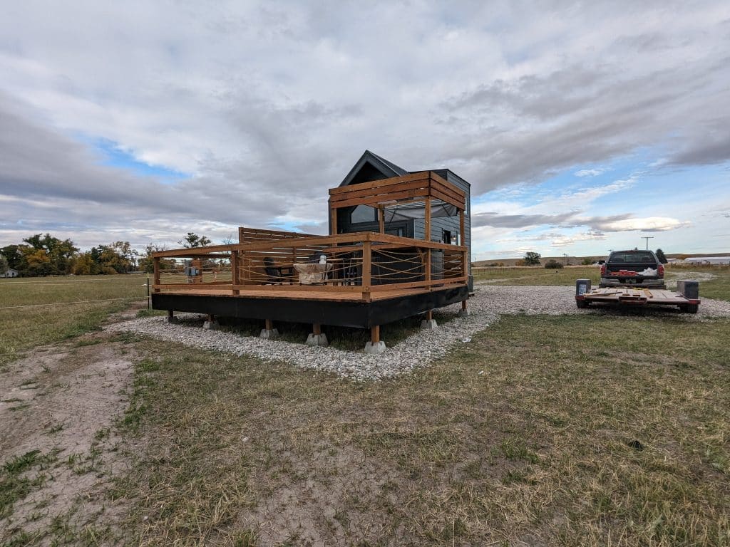 Tiny House Deck Trailer Cloudy Sky Tiny house with a large deck, truck and trailer in the background.